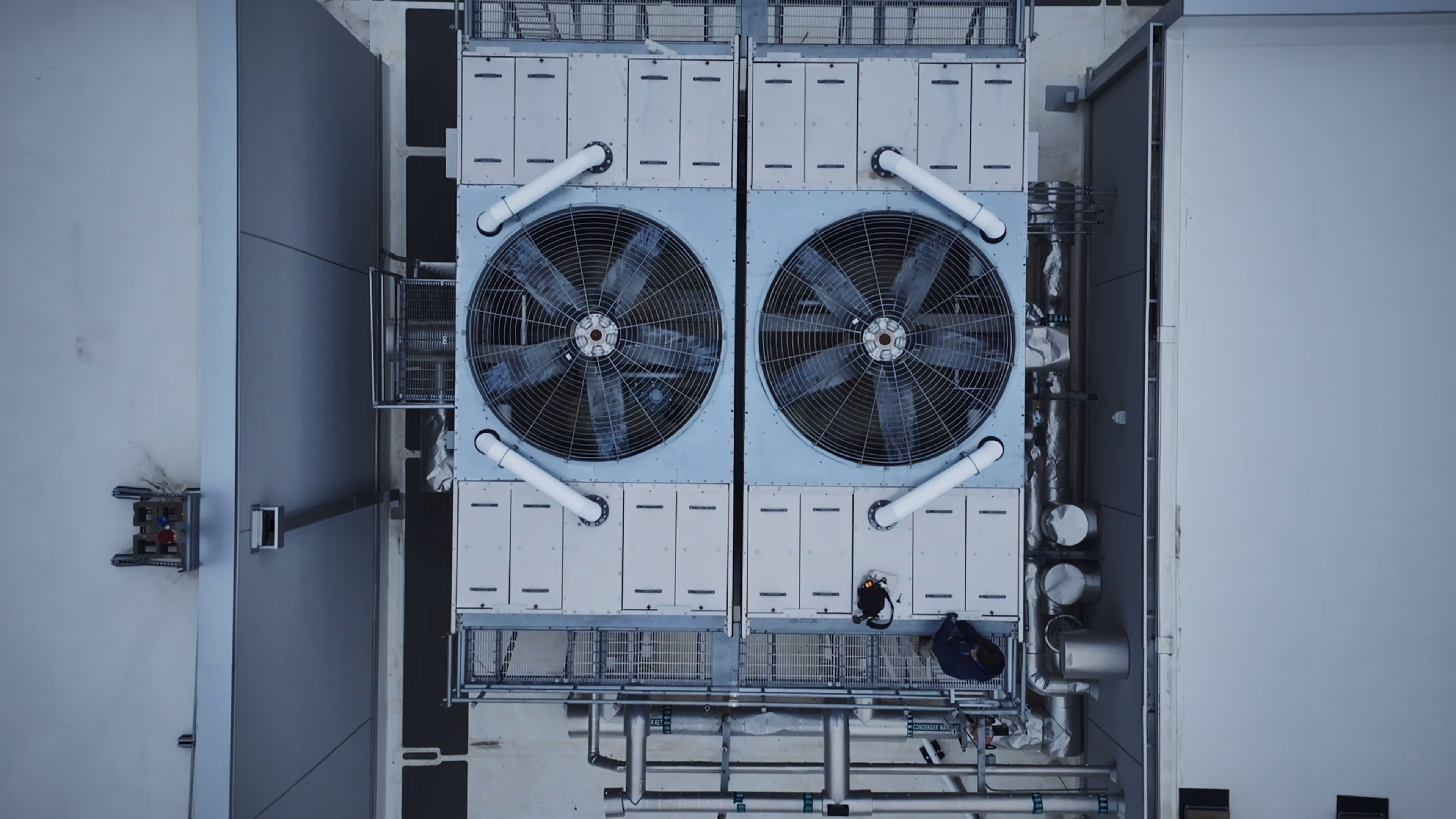 Overhead view of two large industrial cooling fans on a rooftop with a person nearby.