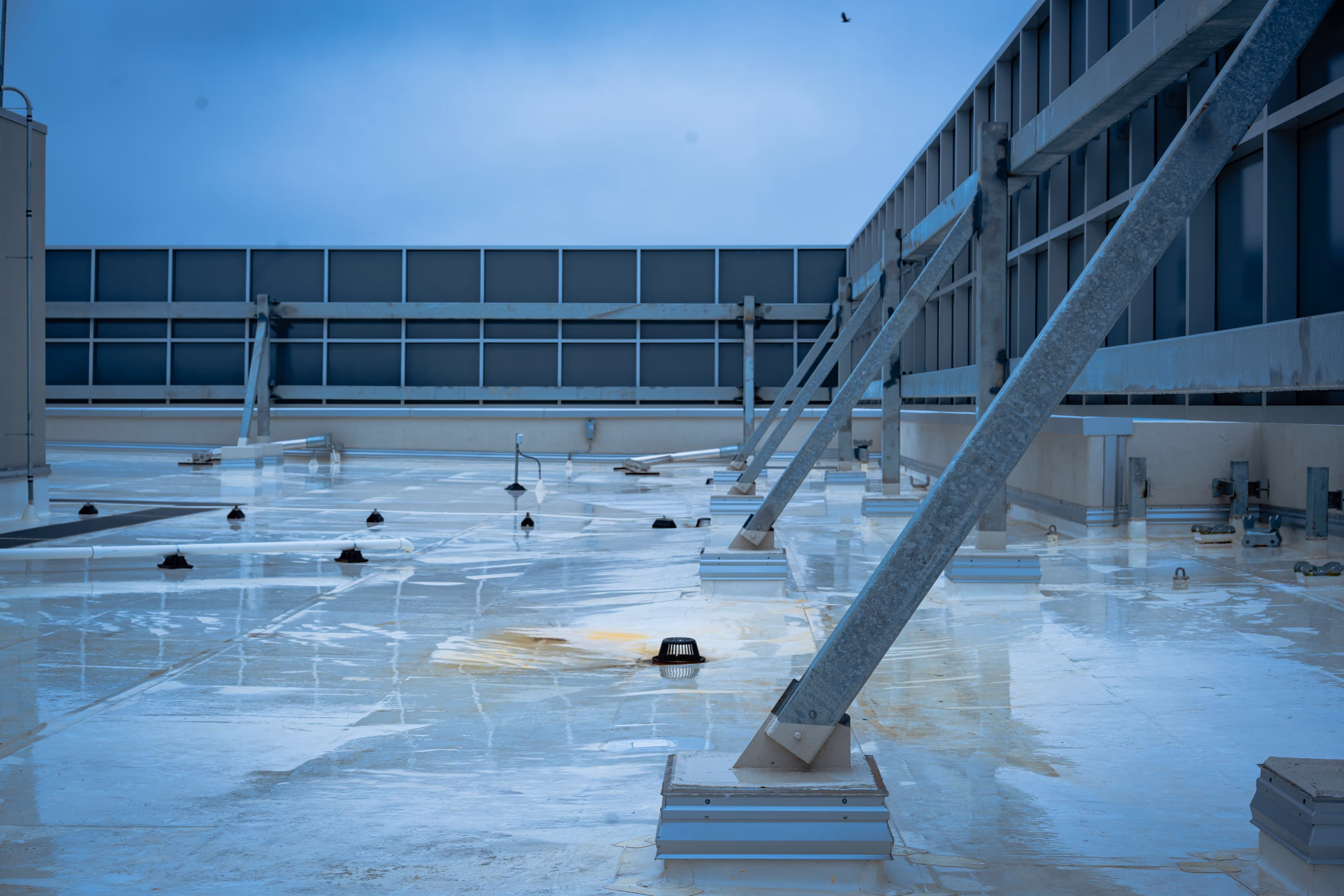 Wet flat rooftop with metal supports and a cloudy blue sky above.