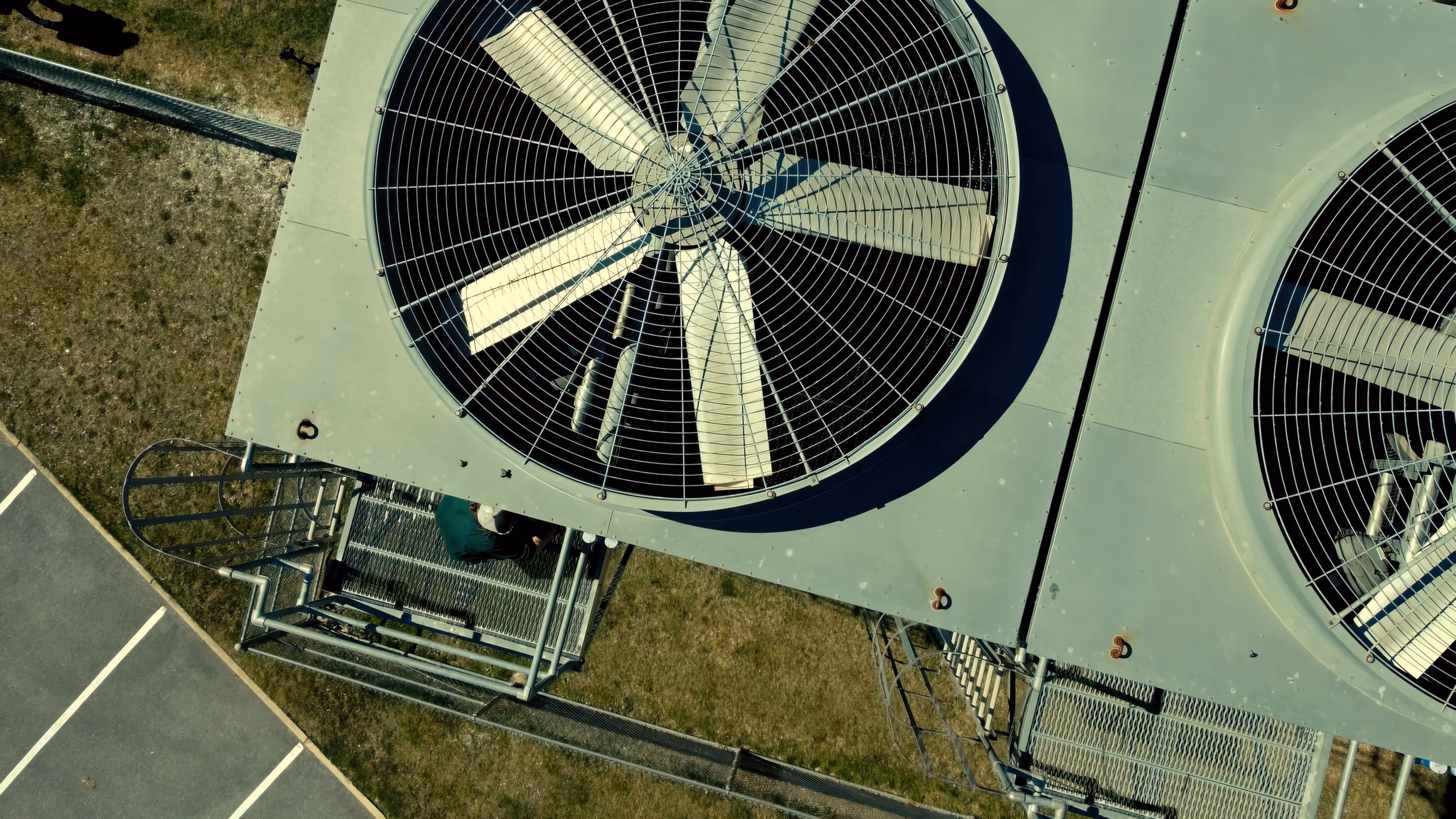 Two large industrial cooling fans on rooftop with a person working on metal grates below.