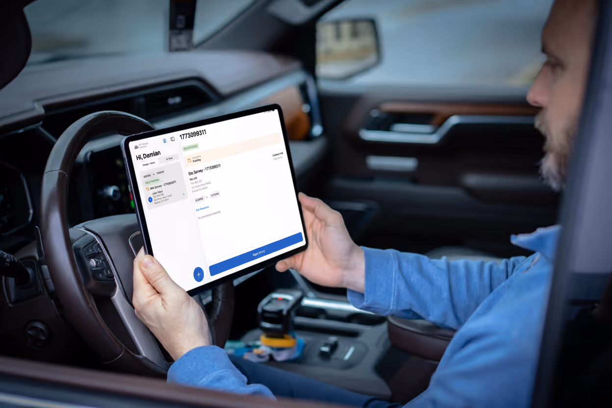 Man seated in a vehicle holding a tablet with an app open displaying delivery details.