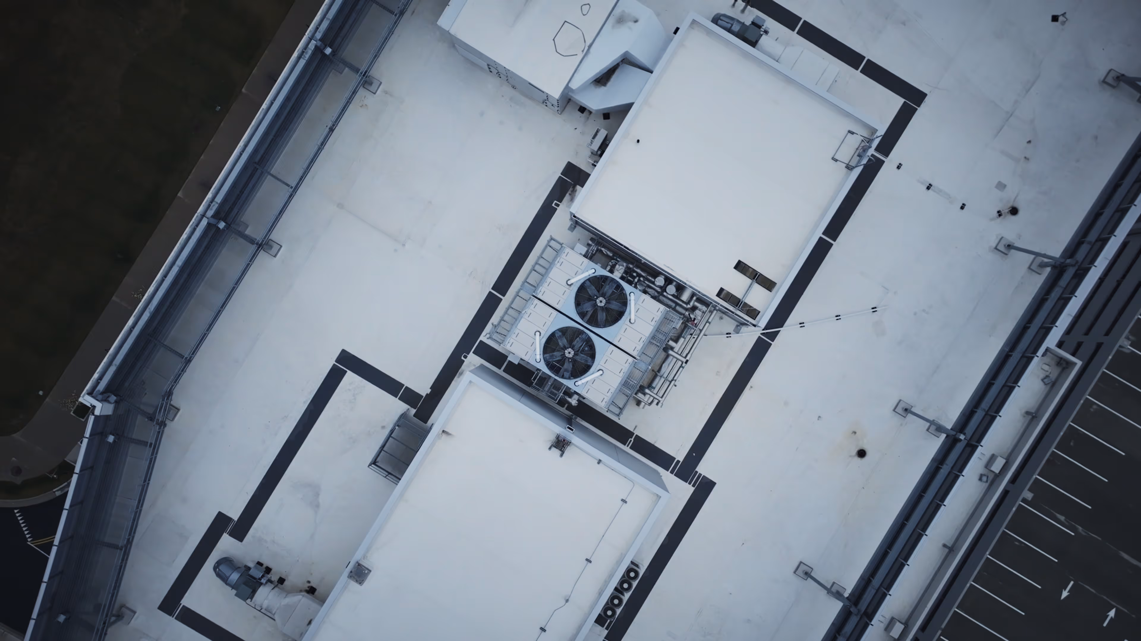 Aerial view of a rooftop with HVAC units and a parking lot alongside it.