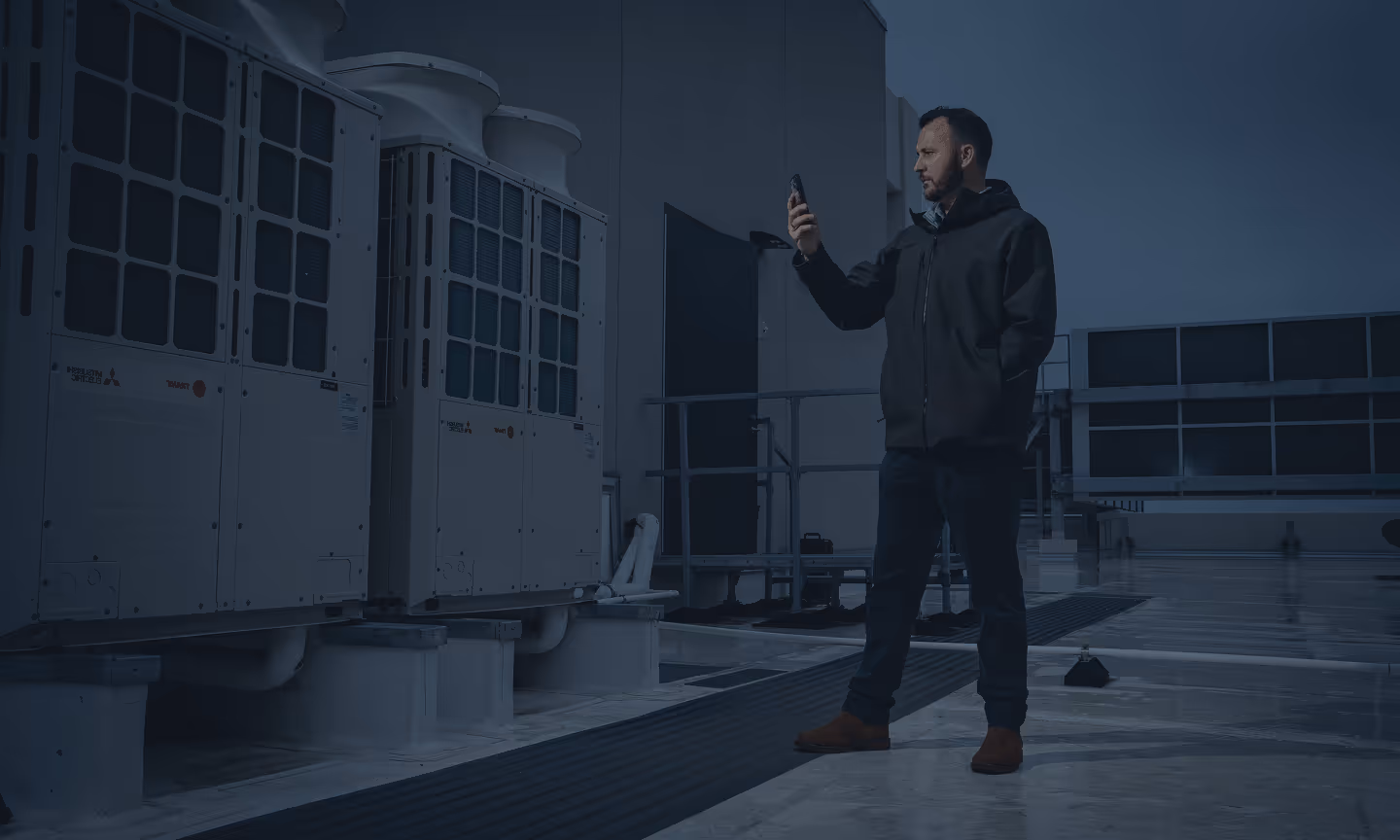 Man inspecting rooftop HVAC units using his smartphone at dusk.