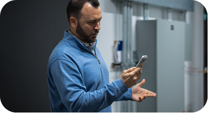 Man in blue jacket looking at his smartphone with a confused expression indoors.