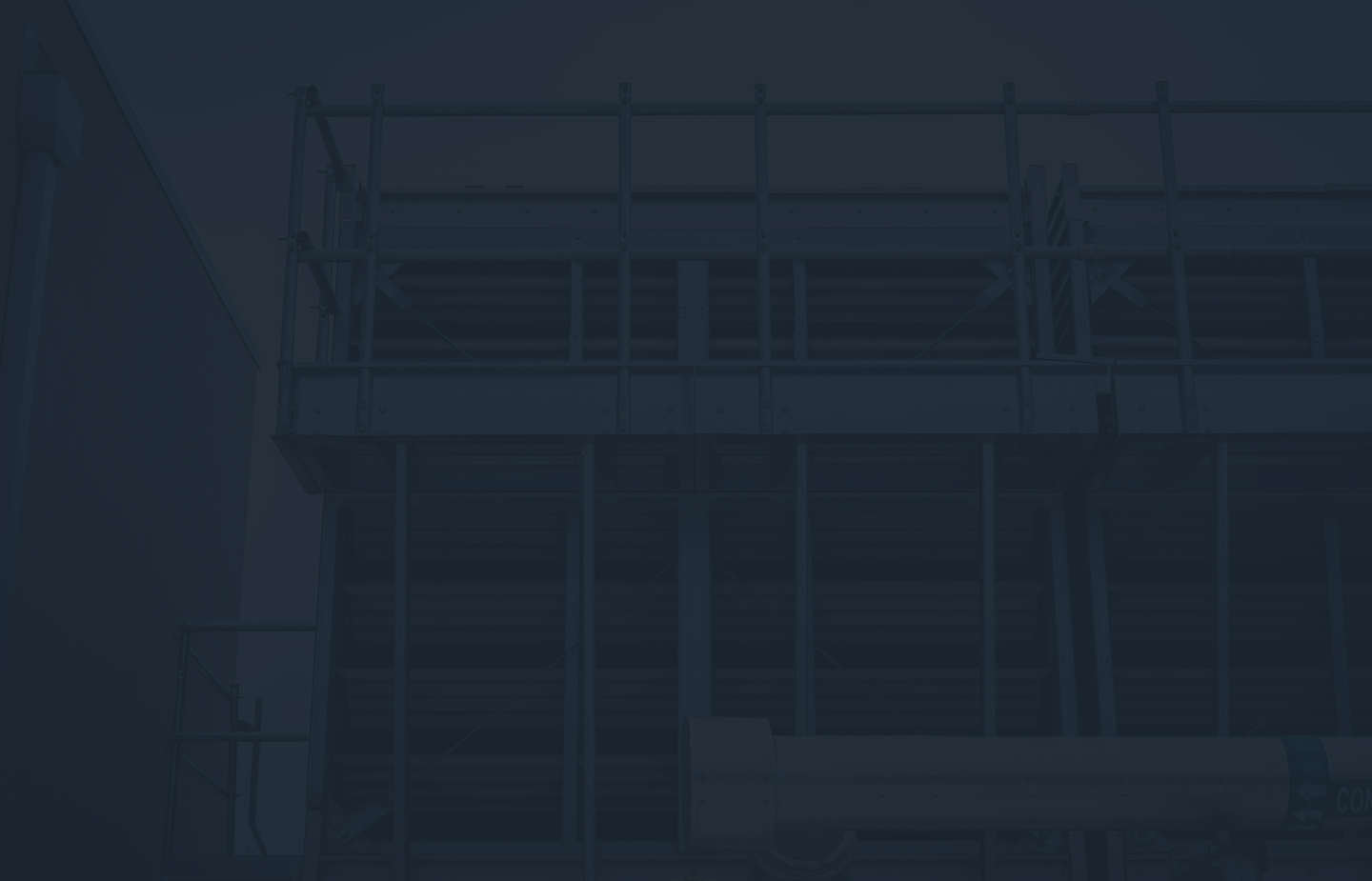 Industrial metal scaffolding and piping against a building exterior under a dark overlay.