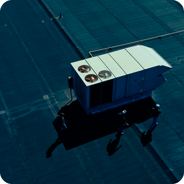 Three people walking on a rooftop near a large HVAC unit casting long shadows.