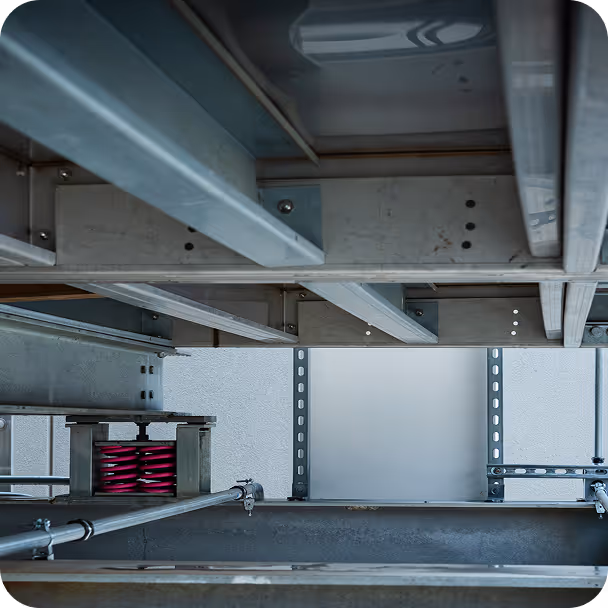 Industrial metal framework and beams with a visible red spring component mounted on a pipe.