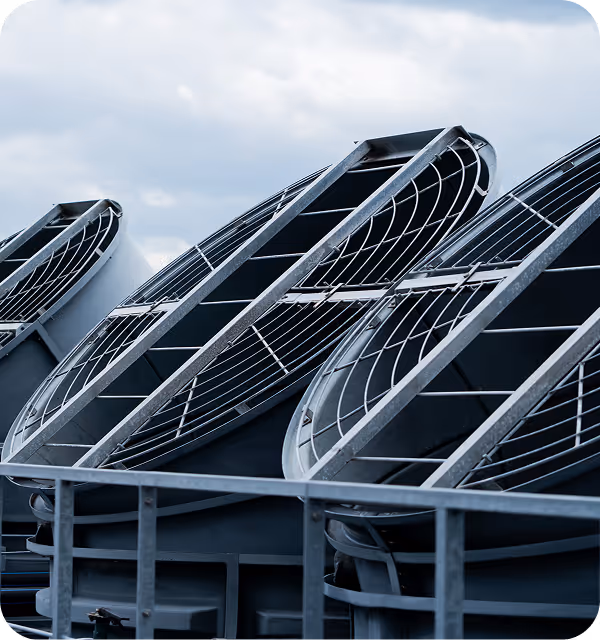 Close-up of large angled metal industrial fans with protective grills against cloudy sky.