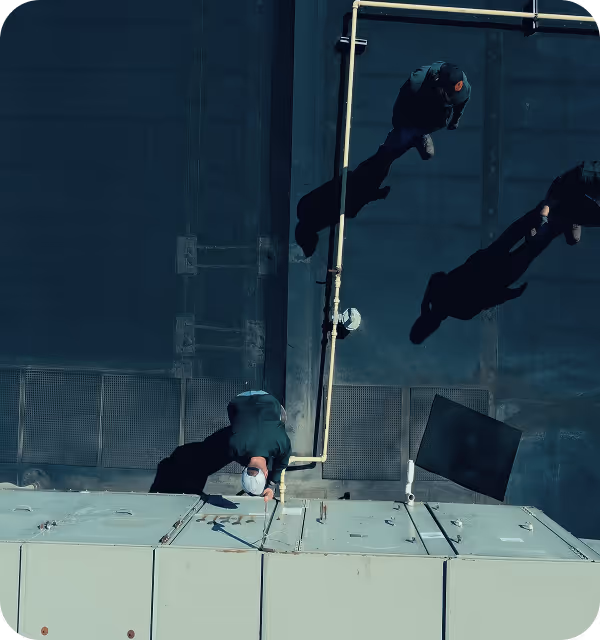 Aerial view of three people walking on a rooftop casting long shadows under bright light.