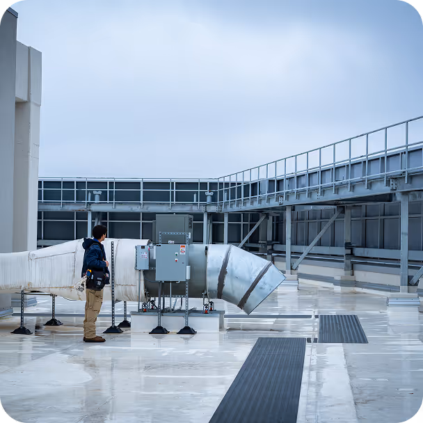 Technician inspecting large industrial ventilation ducts on a rooftop with metal walkways.