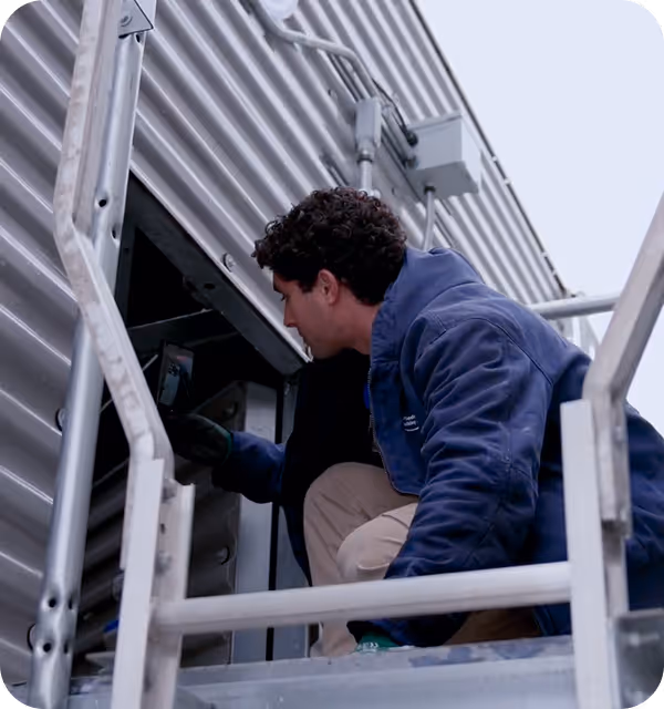Technician in blue jacket inspecting equipment inside a metal industrial structure.