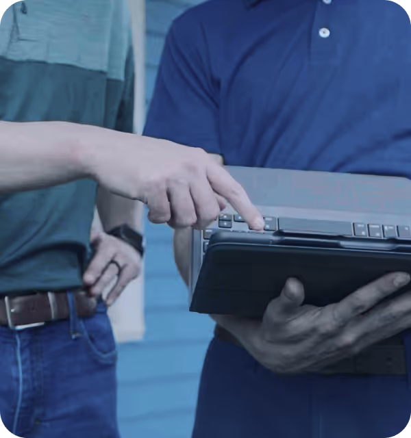 One person pointing at a laptop held by another person wearing a blue shirt.