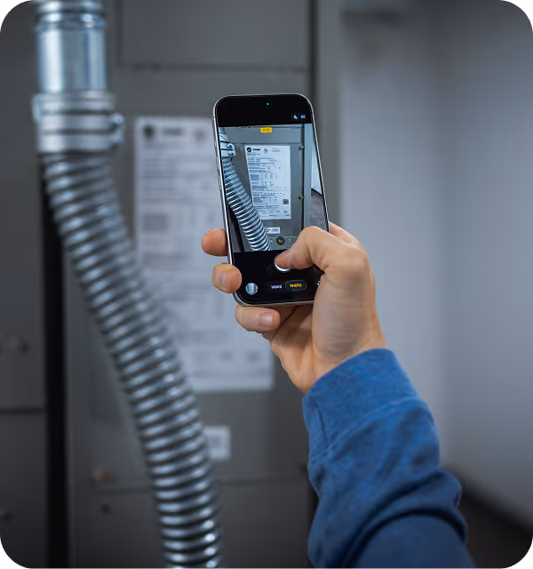 Person in blue sleeve taking a photo of a metal vent and label on a gray machine with a smartphone.