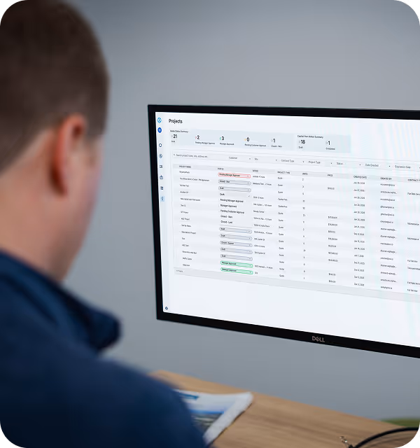 Person viewing a large Dell monitor displaying project management software with a list of tasks and statuses.