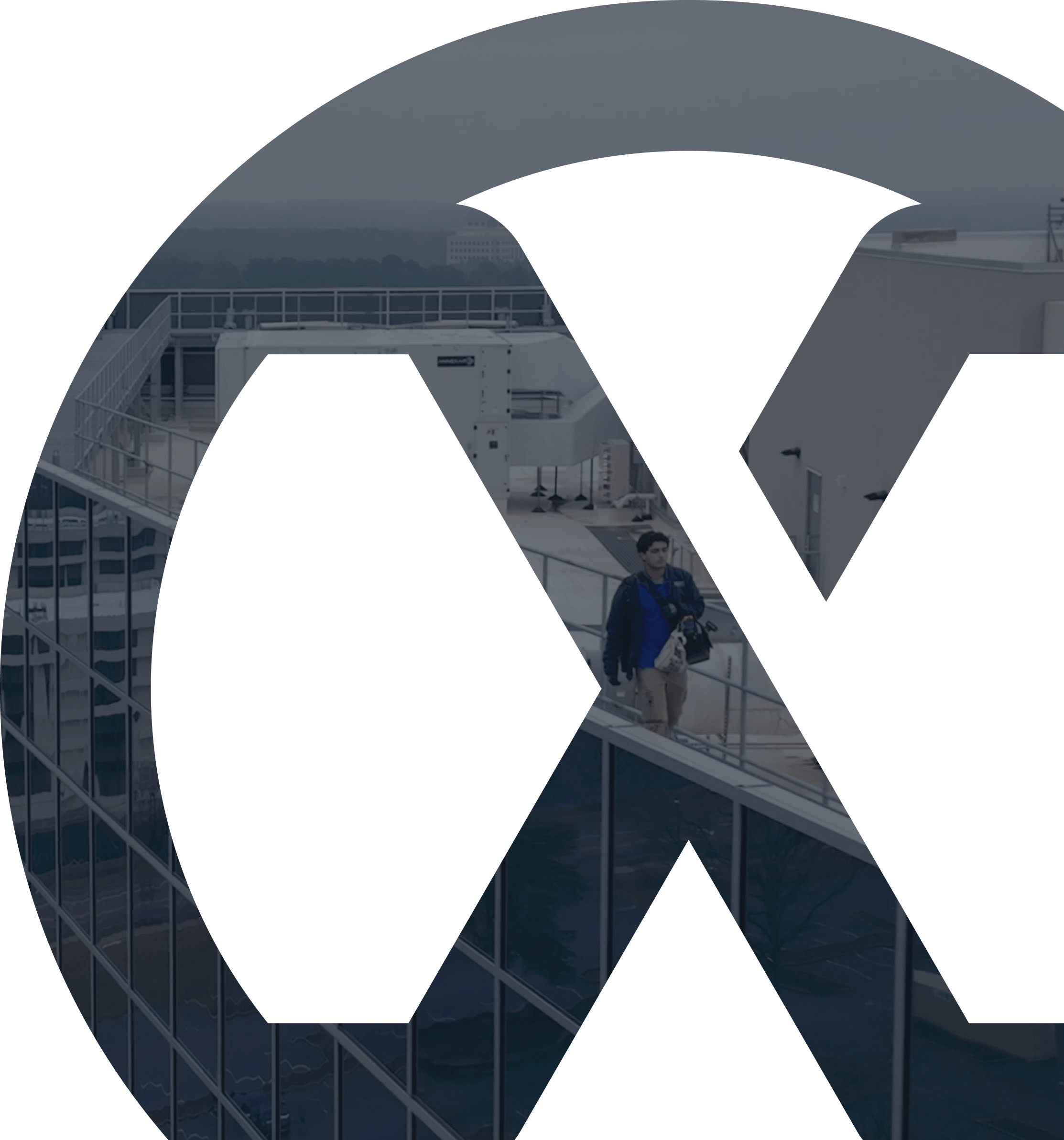Man walking on rooftop walkway of glass building under an overcast sky.