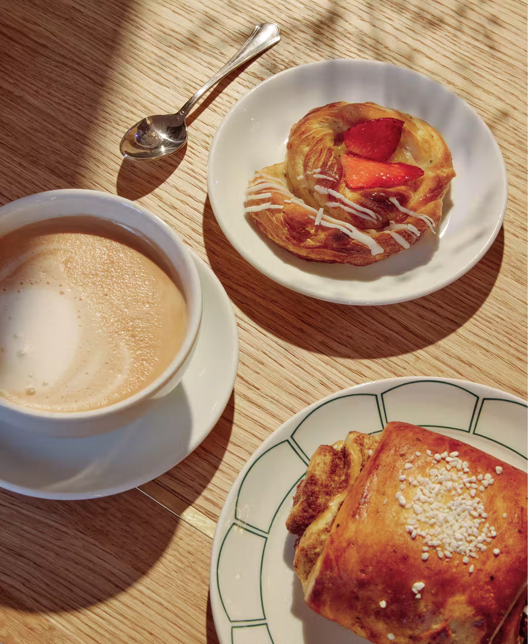 Taulu-kahvilan aamupala – latte, mansikanpulla ja croissant puisella pöydällä aurinkoisessa päivänvalossa