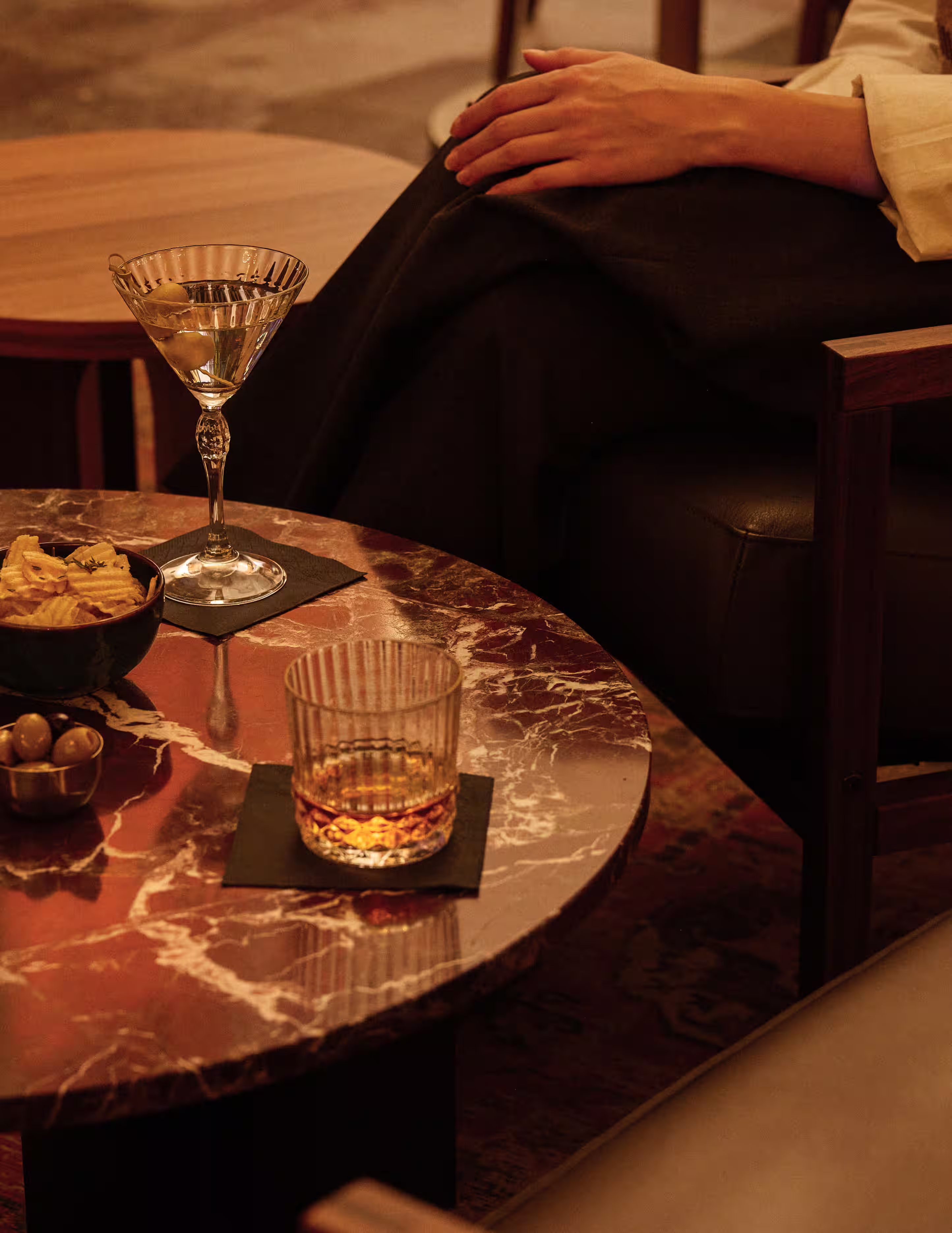 Cocktailtunnelmaa Taulu-baarissa – martini ja viskilasi punaisella marmoripöydällä, rentoilu nahkatuolissa