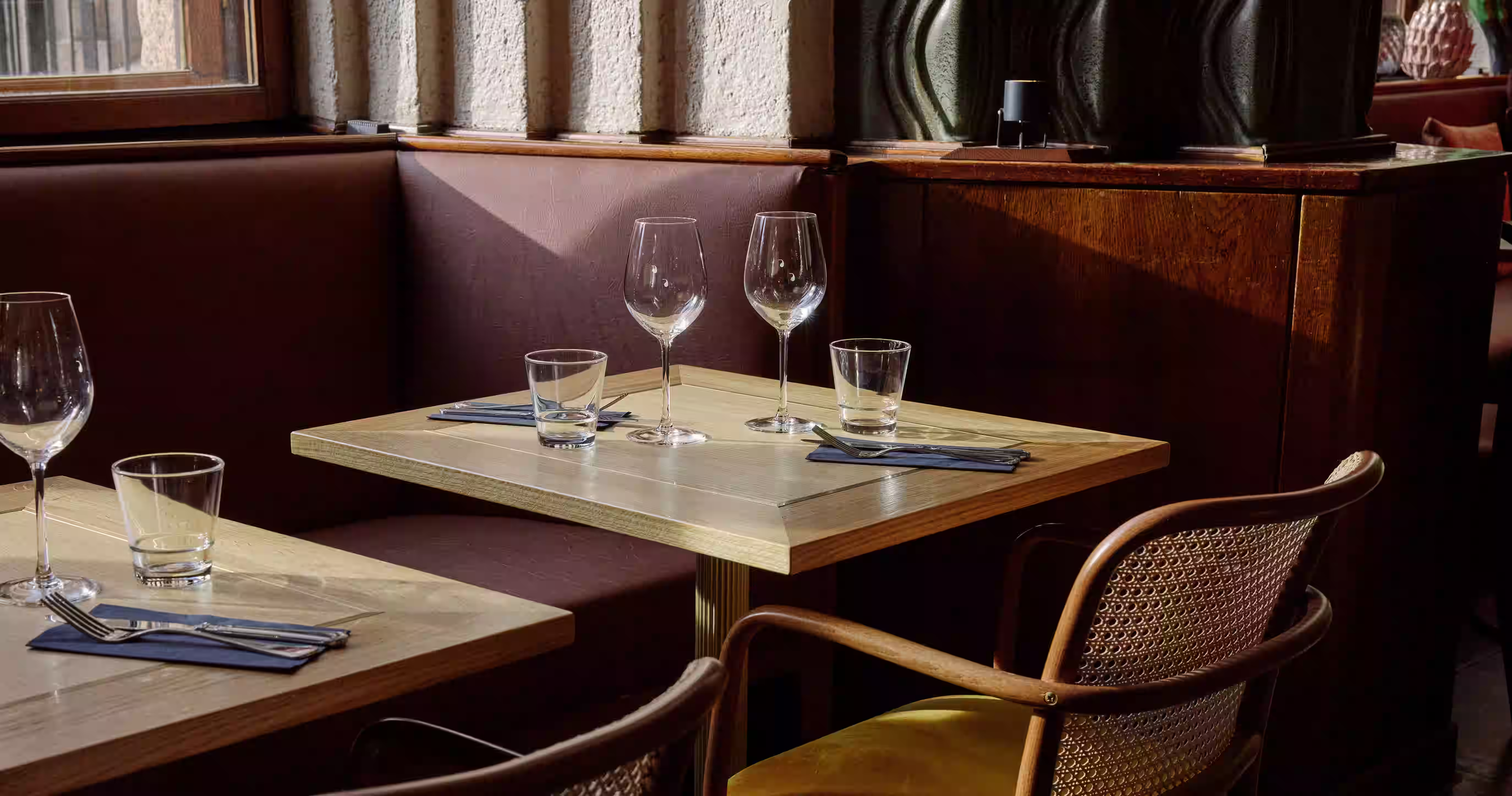 Ravintola Taulun elegantit ruokailupöydät – viinilasit katettuina, rottinkituolit ja tummanpunainen sohvapenkki jugendilaisten yksityiskohtien välissä
