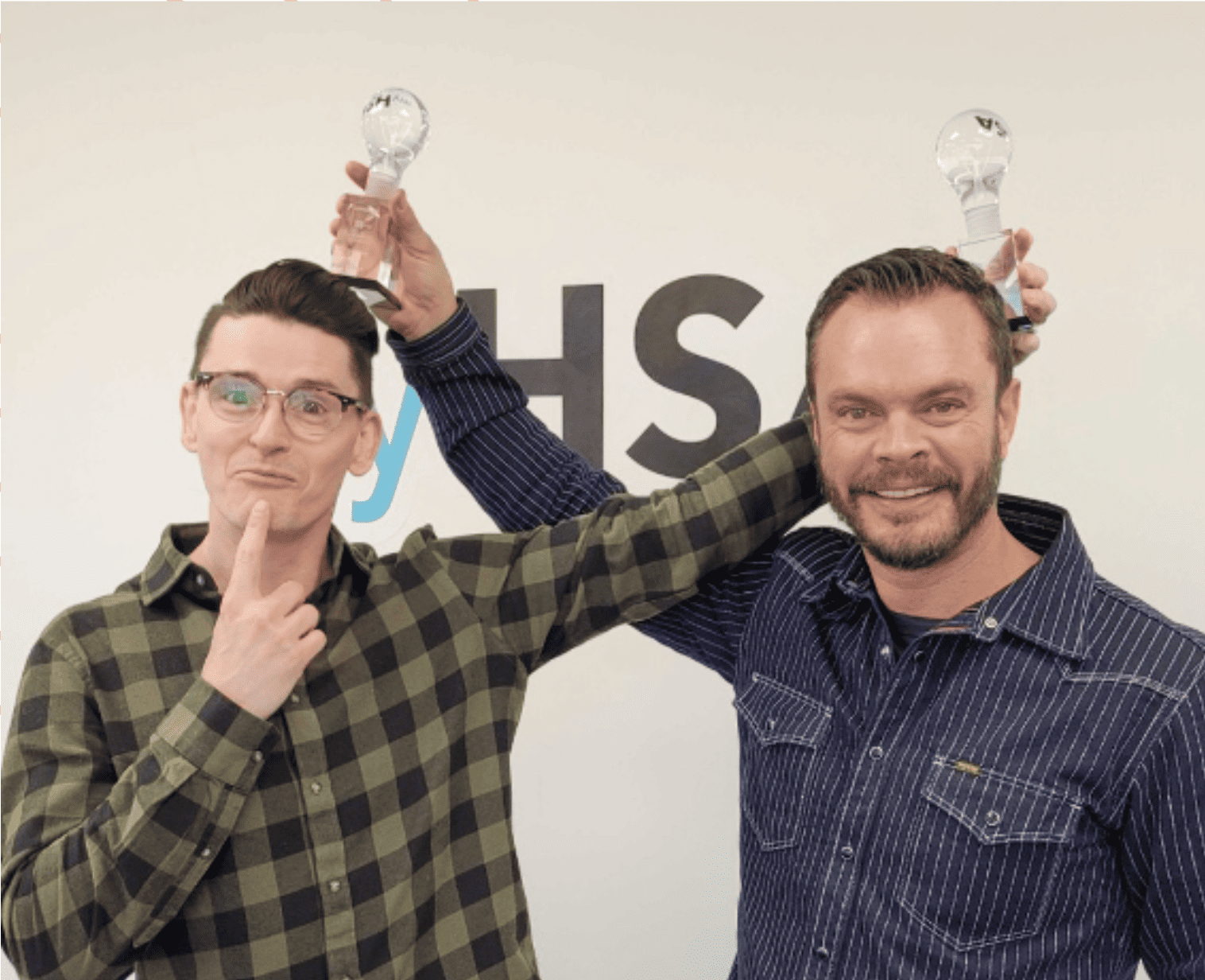 Two men smiling and playfully holding lightbulb-shaped awards above each other's heads.