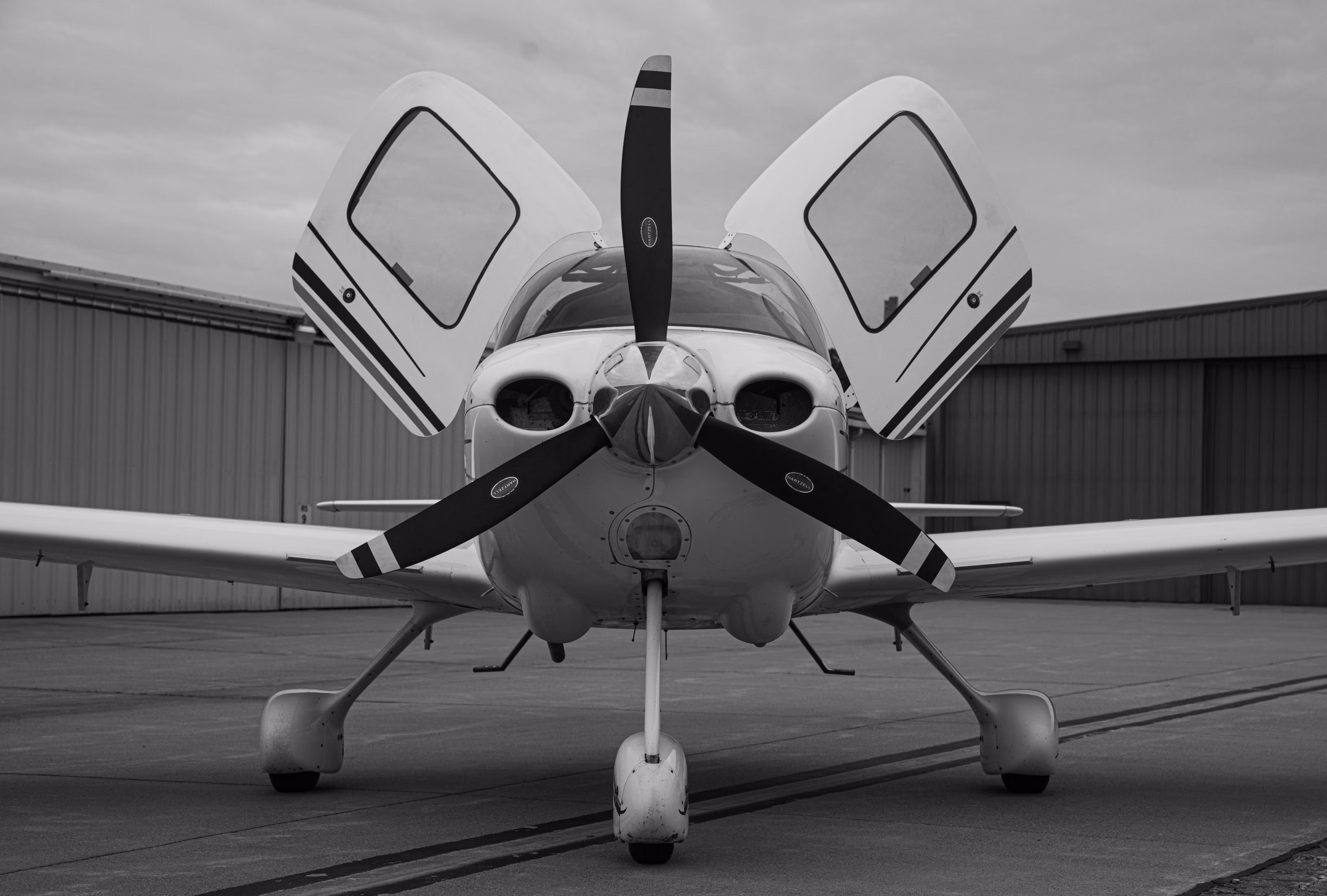 Front view of a small airplane with open doors and propeller on a tarmac.