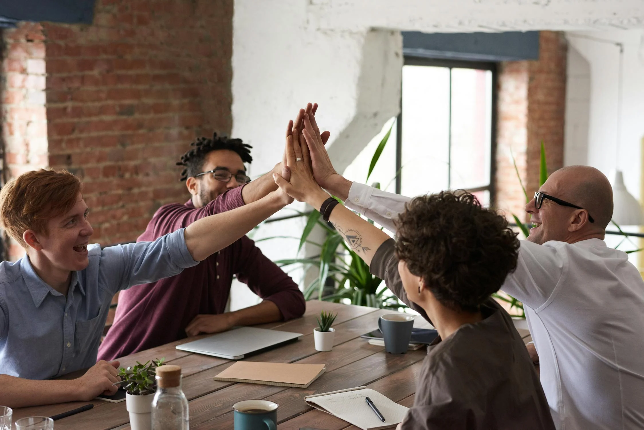 group of colleagues sitting at a table while high fiving each other