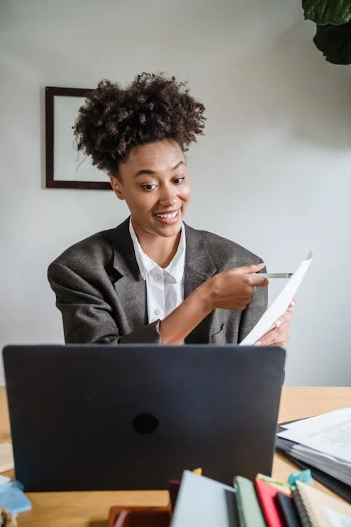 woman sitting at computer pointing to a sheet of paper