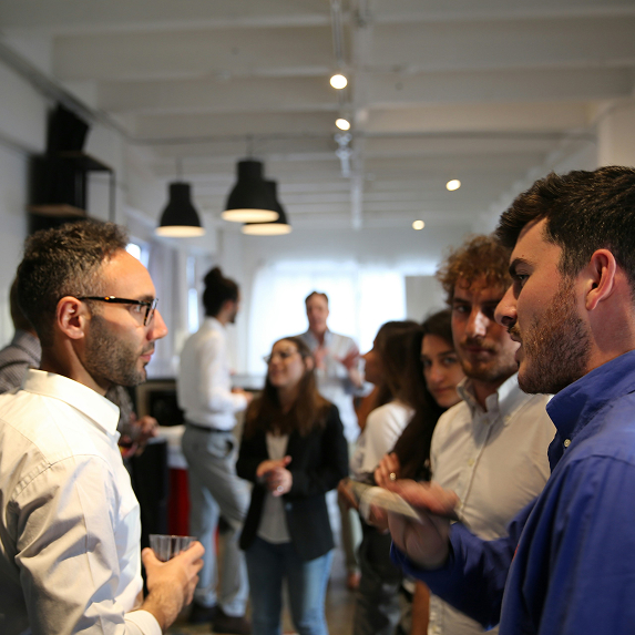 Group of young adults engaged in conversation at an indoor social gathering.