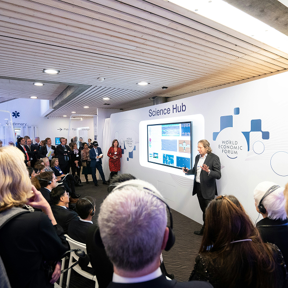 Speaker presenting scientific information on a digital screen labeled Science Hub to an audience at the World Economic Forum.