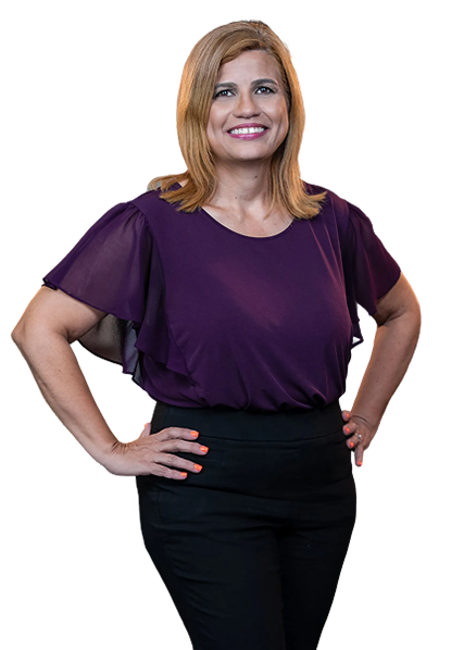 Smiling woman with shoulder-length blonde hair wearing a purple blouse and black pants, standing with hands on hips.