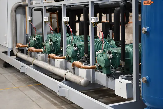 Cuatro compresores verdes conectados con tuberías de cobre y negro en un equipo industrial.
