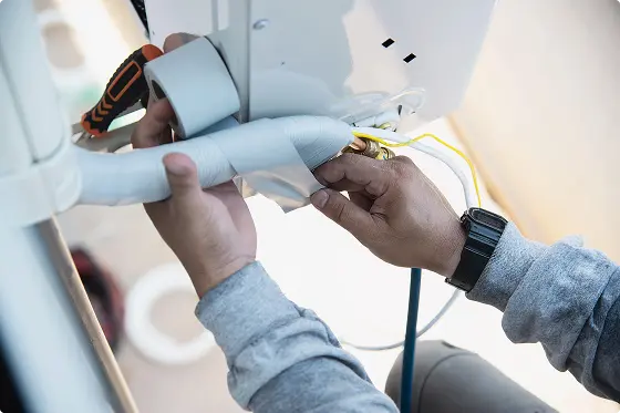 Manos instalando tubería aislada con cinta blanca y cables eléctricos en un aparato blanco.