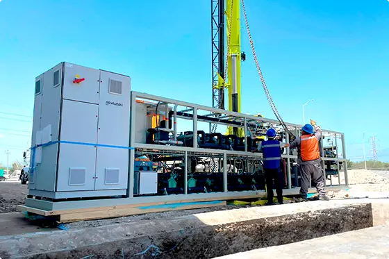 Dos trabajadores con cascos instalan equipo mecánico grande en una obra al aire libre.