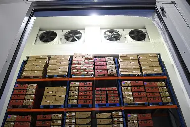 Estantería alta con cajas apiladas y ventiladores en la parte superior en un almacén refrigerado.