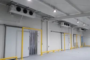 Pasillo industrial con puertas blancas y marcos amarillos bajo ventilación en techo gris.