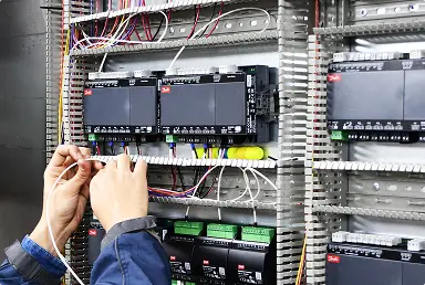 Manos conectando cables eléctricos en panel de control industrial con módulos y circuitos.