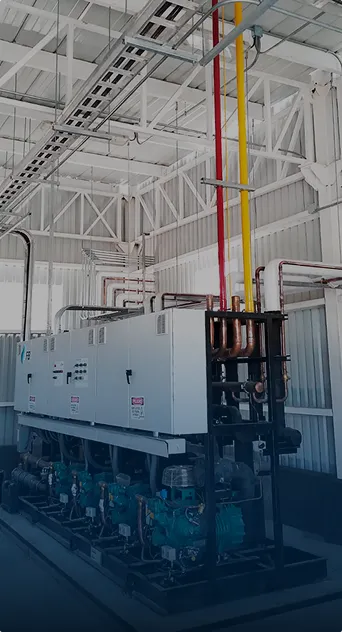 Máquina industrial con tuberías y cables en un espacio cerrado con techo y paredes blancas.
