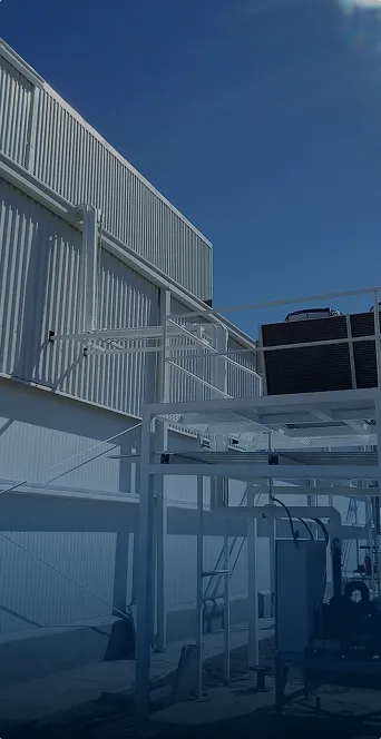 Instalación industrial metálica blanca con maquinaria y estructura bajo un cielo azul despejado.