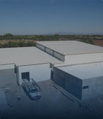 Construcción de edificio blanco con techo plano en área rural con vegetación y cielo claro.