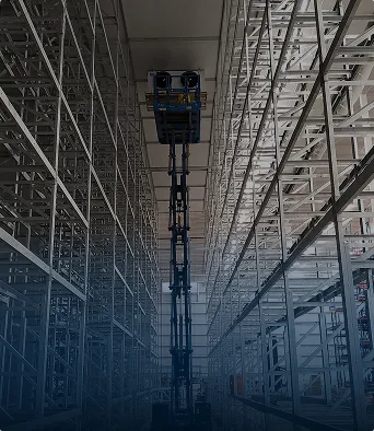 Plataforma elevadora entre estanterías metálicas en construcción de almacén grande.