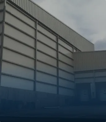 Exterior of a large industrial warehouse building with metal siding under a cloudy sky.