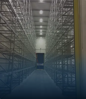 Estantes altos y vacíos en un centro de distribución con un pasillo central iluminado.