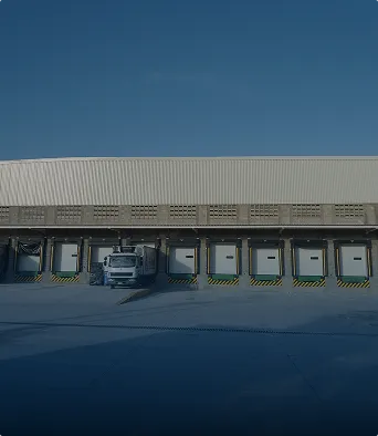 Camión estacionado frente a muelles de carga en un almacén industrial bajo un cielo azul.