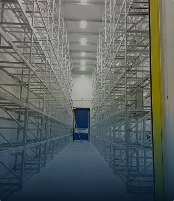 Interior de un cuarto frío vacío con estanterías metálicas y puerta azul al fondo.