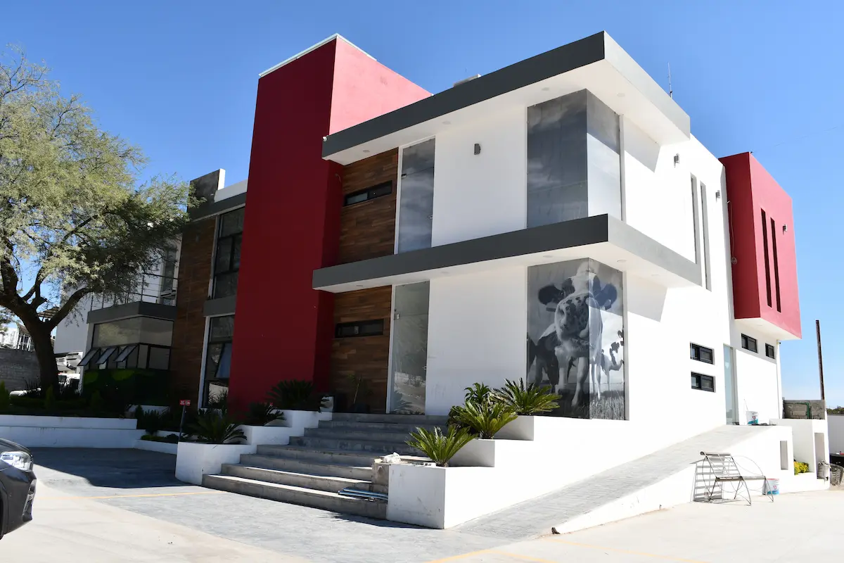 Casa moderna de dos pisos con paredes blancas y detalles rojos, escaleras y rampas de acceso.