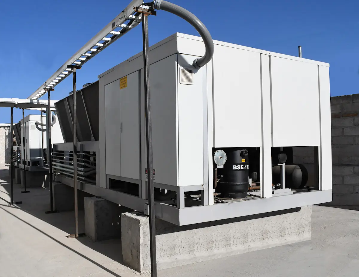 Unidad de aire acondicionado industrial blanca instalada sobre base de concreto exterior bajo cielo despejado.