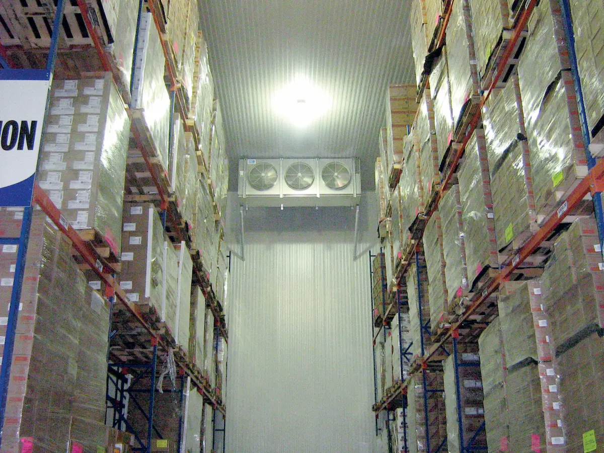 Almacén con estanterías altas llenas de cajas apiladas y un sistema de ventilación en el techo.