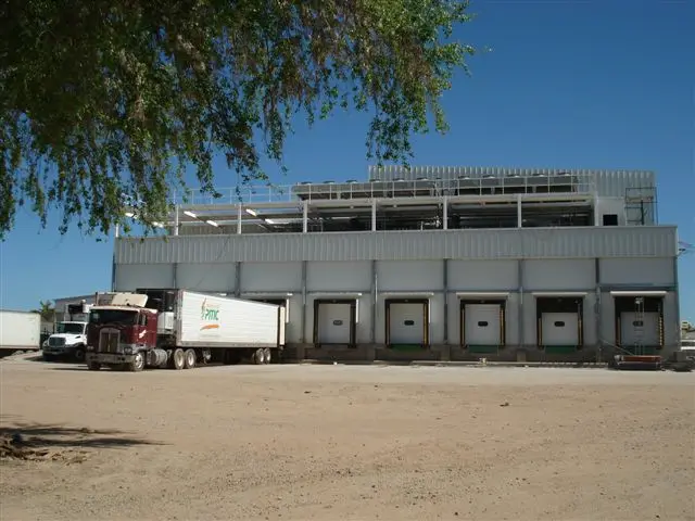 Camión de carga estacionado en un muelle de descarga de un edificio industrial grande bajo un cielo azul.