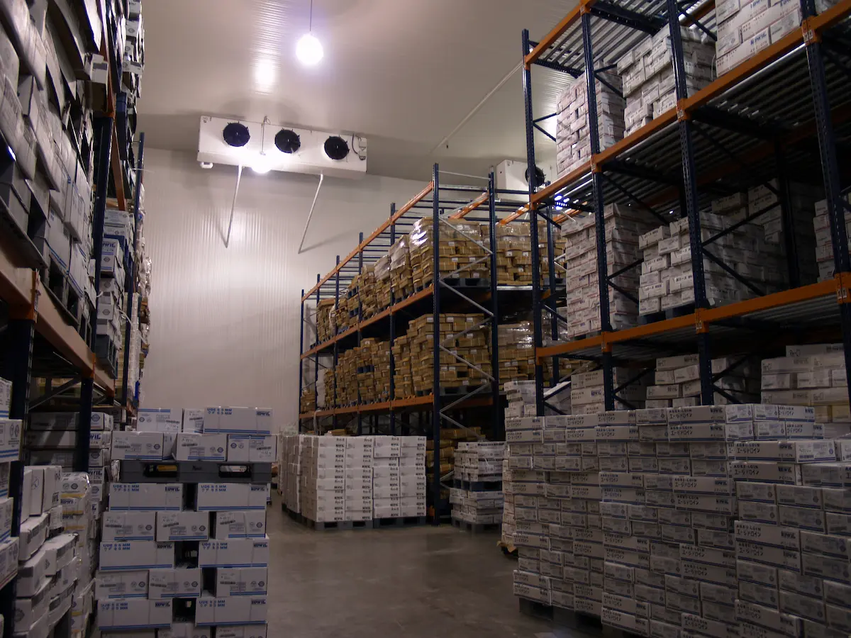 Almacén con estantes llenos de cajas apiladas organizadas en pasillos amplios y techo iluminado.