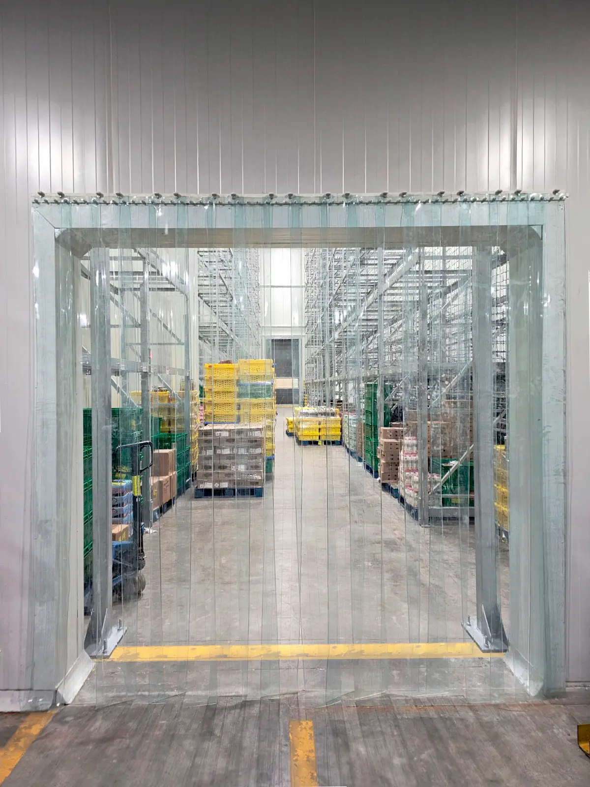 Interior de un almacén con estanterías metálicas y cajas apiladas, vista a través de una cortina plástica.