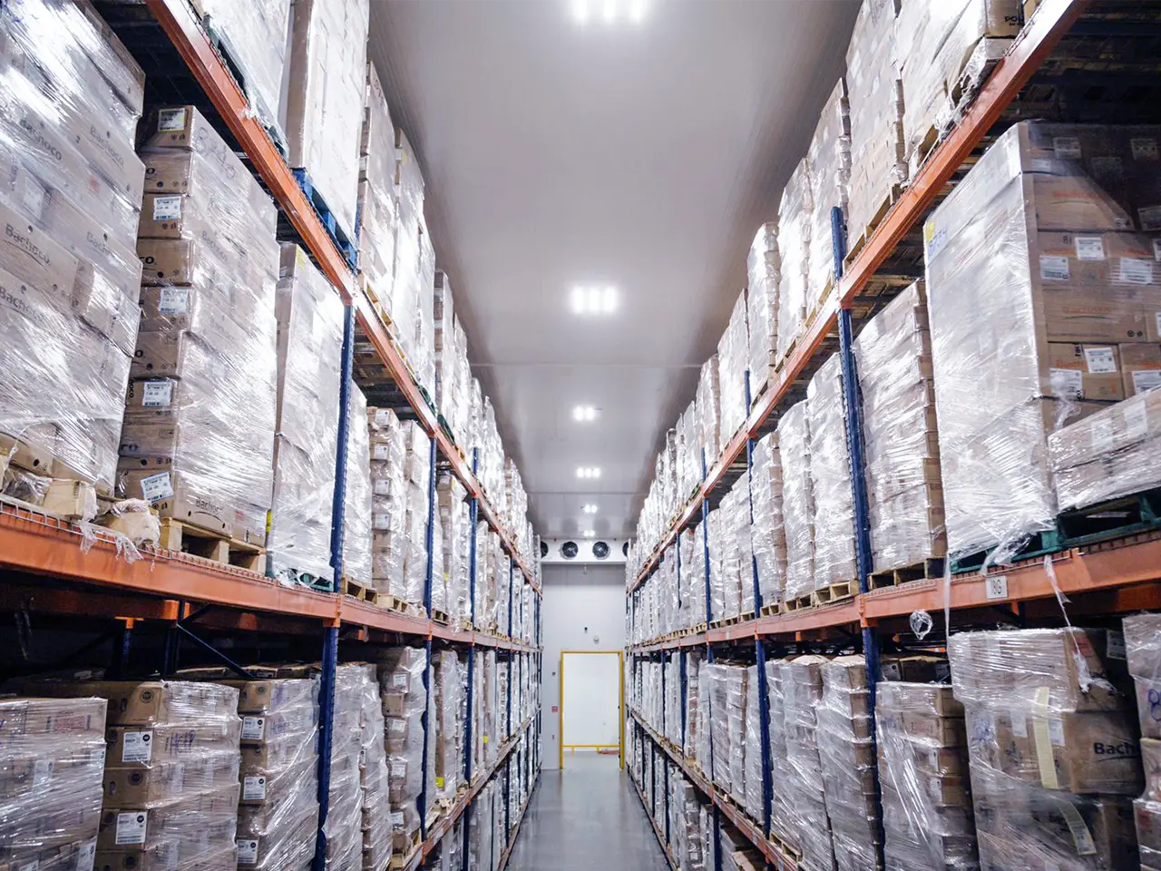 Pasillo de almacén con estantes llenos de cajas embaladas y apiladas hasta el techo.