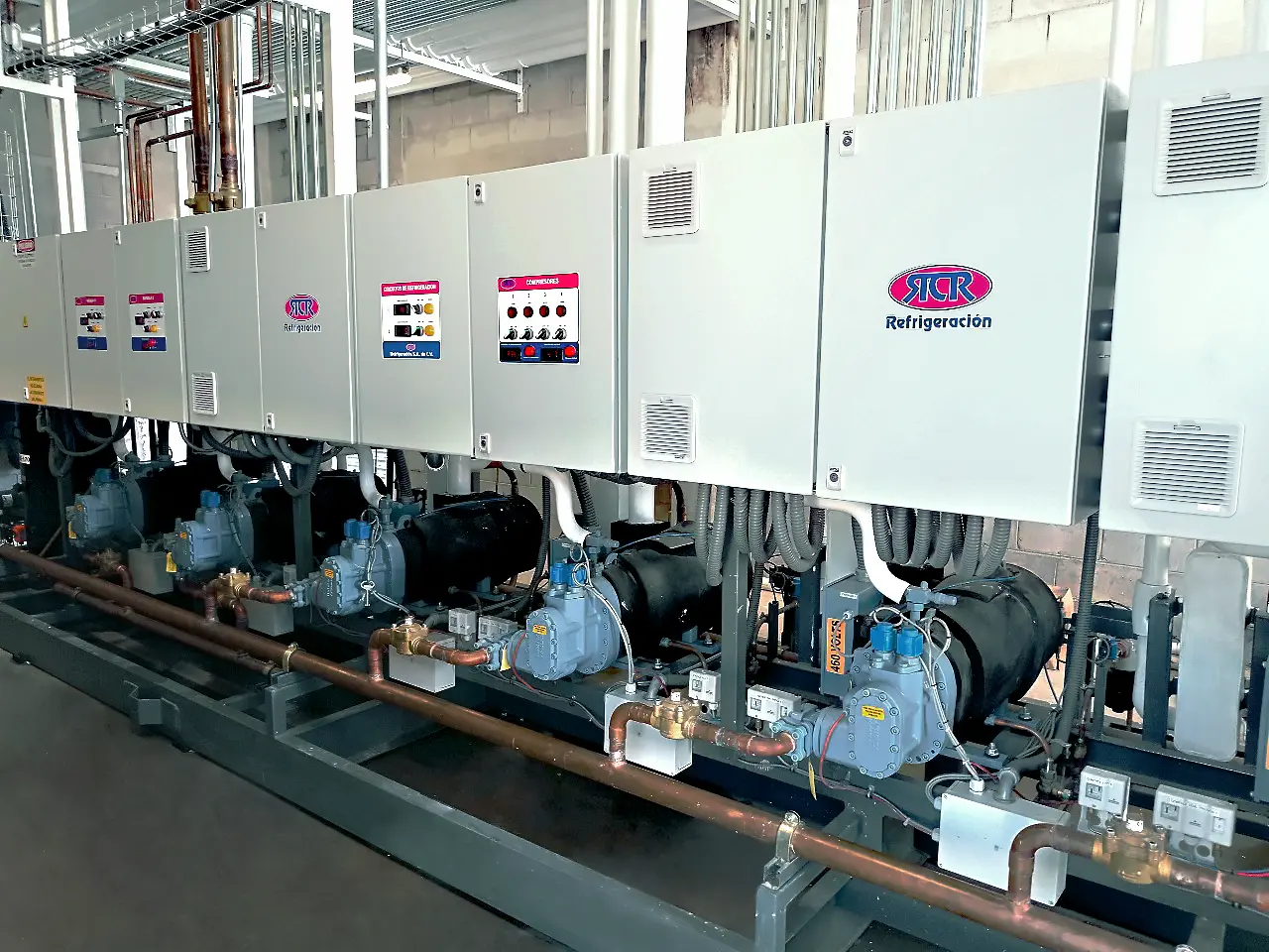 Sistema industrial de refrigeración con múltiples compresores y tuberías de cobre instalados en fila.